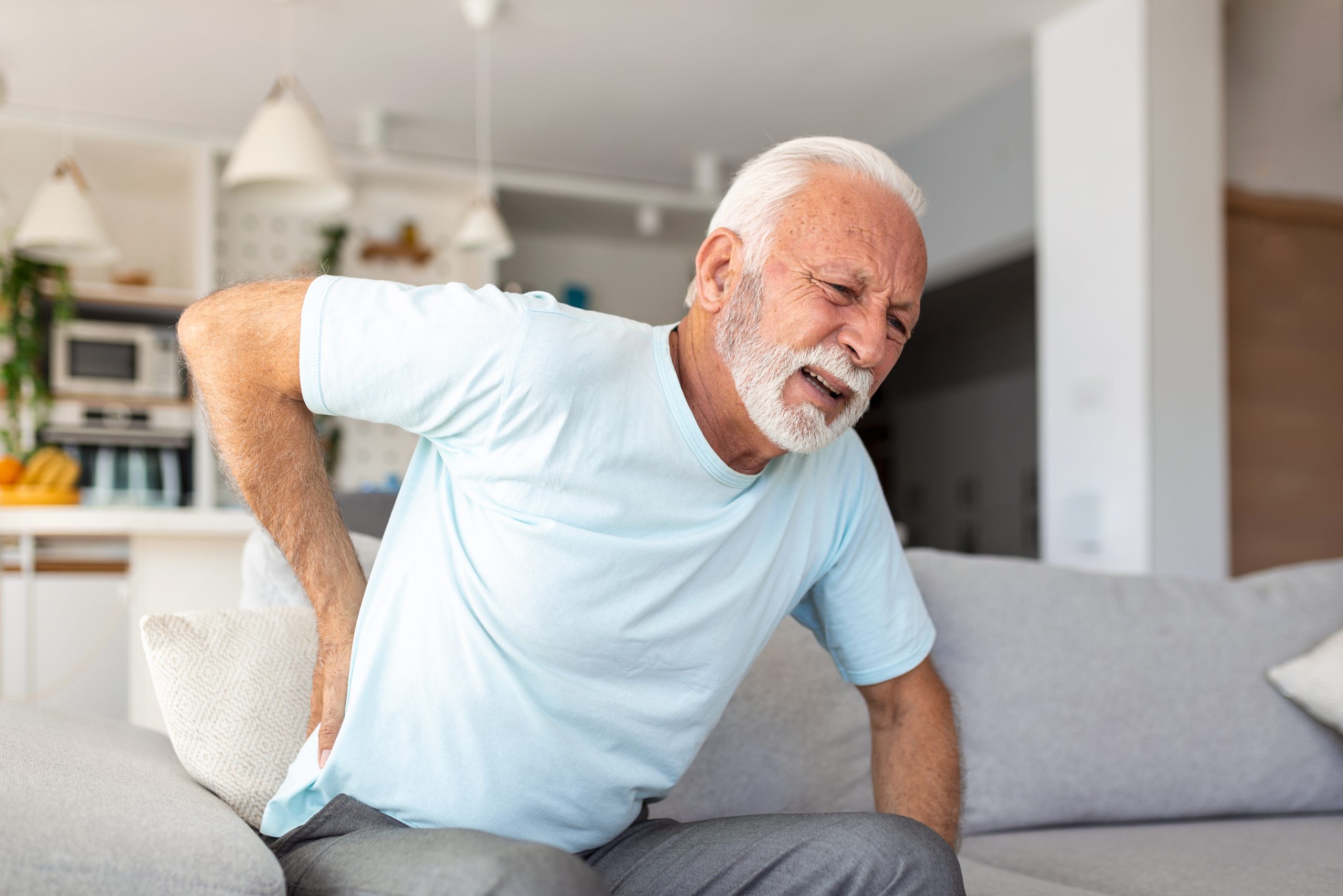 Senior elderly man touching his back, suffering from backpain, sciatica, sedentary lifestyle concept. Spine health problems. Healthcare, insurance